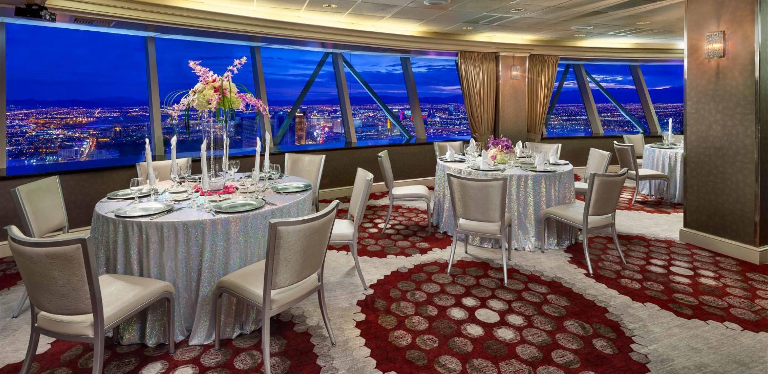 The STRAT SkyPod reception room, the Twilight room, silver tablecloths and white chairs with full table settings and a view of the Las Vegas Strip at night