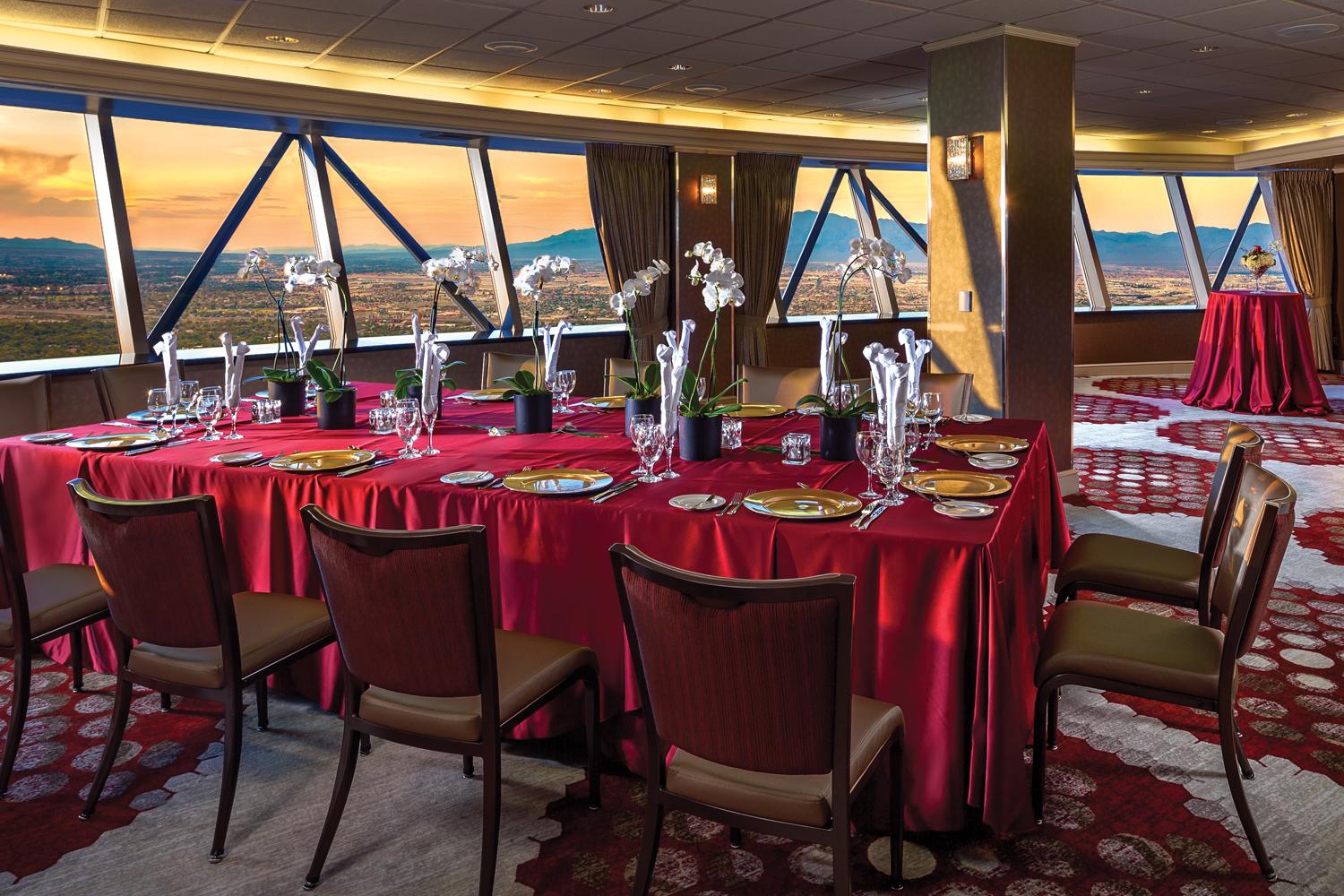 The STRAT SkyPod Horizon Room with a table with red tablecloth and full table set up for dinner and a view of the Las Vegas valley at sunset out the windows