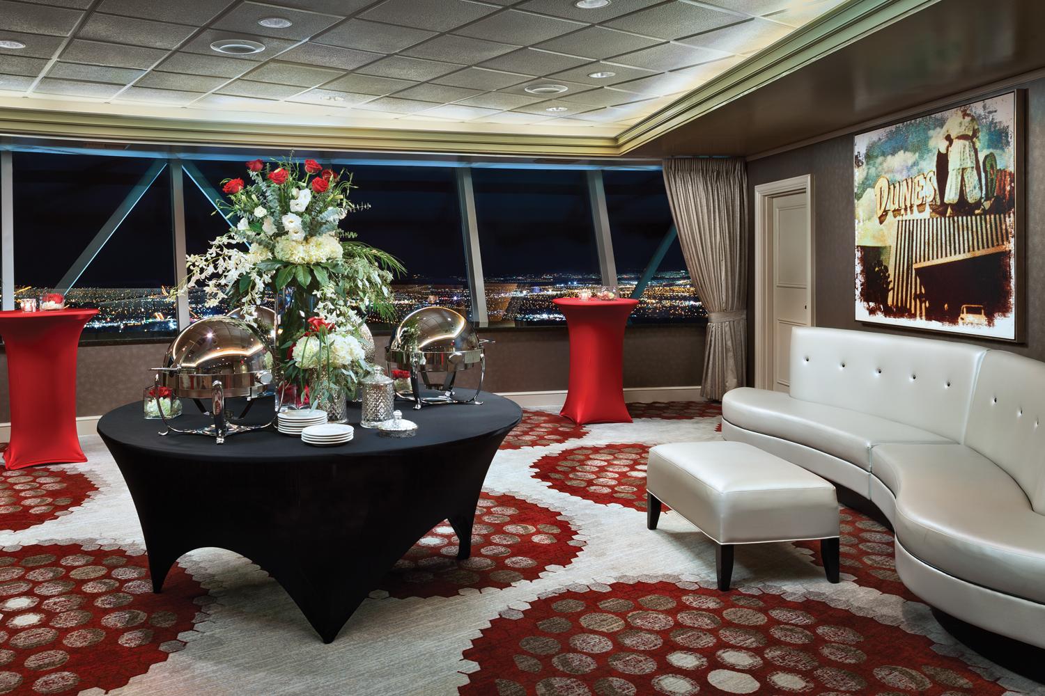 The STRAT Sunrise room in the SkyPod Tower with red and white carpet and a white couch and table with flowers and serving dishes